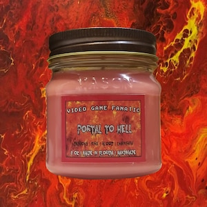 May include: A pink glass jar candle with a brown lid. The label reads "VIDEO GAME FANATIC PORTAL TO HELL DEMONS I FIRE I BLOOD I CHAINSAW 8 OZ I MADE IN FLORIDA I HANDMADE".