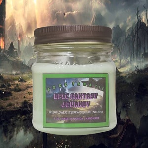 May include: A white candle in a clear glass jar with a brown lid. The label reads "BOOKFANATIC EPIC FANTASY JOURNEY FRESH FLOWERS | CEDARWOOD | FALLEN LEAVES 8 OZ | MADE IN FLORIDA | HANDMADE".