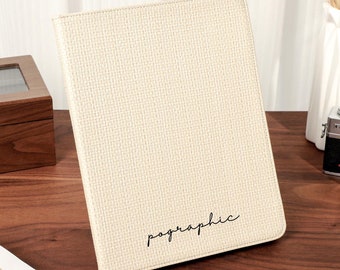 May include: A beige fabric-covered notebook with the word "pographic" written in black cursive on the front.