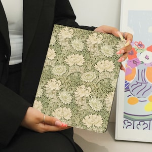 Könnte beinhalten: Eine grüne und weiße Laptoptasche mit floralem Muster und dezentem Glanz. Die Tasche wird in der Hand einer Person gehalten.