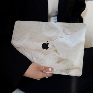 May include: A laptop computer with a marble-patterned skin. The laptop is closed and being held by a person.