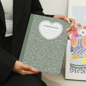 May include: A green composition notebook with a white heart shape on the front. The heart has the word "COMPOSITION" printed inside.