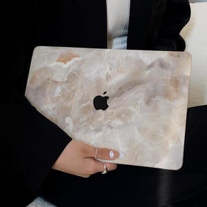 May include: A laptop computer with a marble-patterned skin. The laptop is closed and has an Apple logo on the lid.