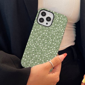 May include: A green phone case with a white floral pattern. The case has a camera lens cutout and a raised lip around the edges.