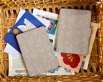 May include: Two beige floral patterned Kindle e-reader covers in a wicker basket with various papers and a pink and red card with a flower design.