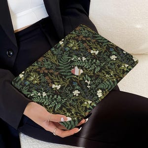 May include: A black laptop skin with a floral pattern featuring green leaves, white flowers, and brown accents. The design is reminiscent of a botanical illustration.