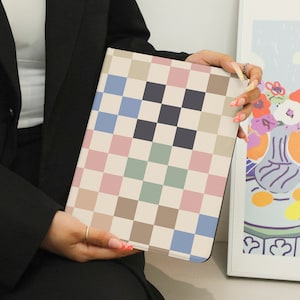 May include: A checkered notebook with a light pink, light blue, light green, and brown pattern. The notebook is closed and held by a person's hand.