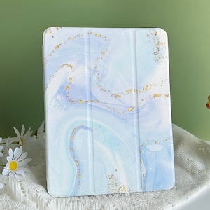 Peut inclure: Une coque pour iPad en marbre bleu et blanc avec des accents dorés. La coque a une surface texturée et un design moderne.