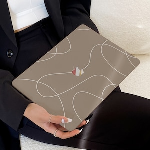 Könnte beinhalten: Eine braune Laptop-Hülle mit einem weißen abstrakten Design. Die Hülle hat einen Ausschnitt für das Apple-Logo.