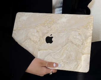 May include: A laptop computer with a white marble design skin. The laptop is closed and being held by a person.