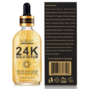 Op de afbeelding: Een gouden fles 24K Gold Serum met een zonafbeelding en de tekst "99,9% puur goud geinfuseerd met Arganolie 100 ml e 3,38 fl.oz". De fles staat op een witte achtergrond. Het product is geformuleerd in Canada.