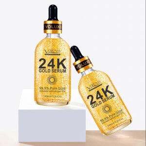 Op de afbeelding: Twee gouden flesjes met 24 karaats Gold Serum, elk met een druppelaar en een etiket met de tekst "VOLUXSS Professional 24K Gold Serum 99.9% Pure Gold Infused with Argan Oil 100ml e 3.38 fl.oz."
