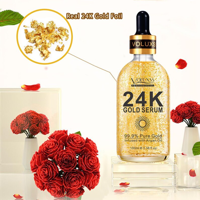 Op de afbeelding: Een gouden fles met een druppelaar en een gouden etiket met de tekst "VOLUXSS PROFESSIONAL 24K GOLD SERUM 99.9% Pure Gold Infused with Argan Oil 100ml e 3.38 fl.oz". De fles staat op een wit oppervlak met rode rozen op de voorgrond.