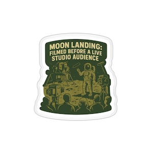 May include: A sticker with a humorous illustration depicting a staged moon landing. The image shows an astronaut, cameras, and an audience, with the text "MOON LANDING: FILMED BEFORE A LIVE STUDIO AUDIENCE" in a green banner.