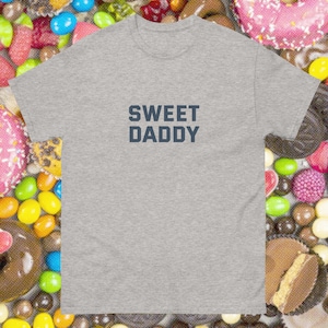 May include: A gray t-shirt with the text "SWEET DADDY" printed in dark blue.