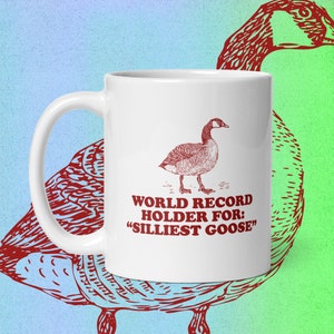May include: White ceramic coffee mug with a red illustration of a goose and the text "WORLD RECORD HOLDER FOR: "SILLIEST GOOSE""
