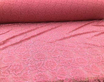 May include: A roll of pink lace fabric with a floral pattern. The fabric is a soft, delicate material with a repeating design of flowers and leaves. The lace is a solid color and appears to be a medium weight.