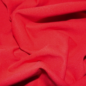 May include: A close-up of a red fabric with a smooth, textured surface. The fabric is folded and draped, creating soft, flowing lines.