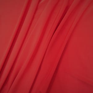 May include: A close-up of a smooth, red fabric with soft folds and wrinkles.