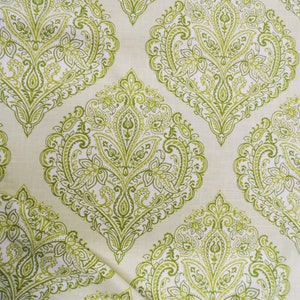 May include: Close-up of a fabric with a repeating pattern of green paisley designs on a cream background. The paisley shapes are detailed with floral and leaf motifs, creating a textured appearance. The fabric has a vintage or retro aesthetic.