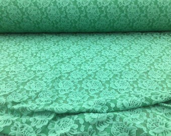 May include: A close-up of a light green fabric with a floral lace pattern.