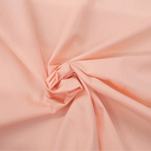 May include: A close-up shot of a peach-colored fabric, artfully arranged with folds and creases. The fabric's texture is smooth, and the lighting creates shadows that accentuate the folds, giving the material a sense of depth and volume. The overall effect is soft and inviting.