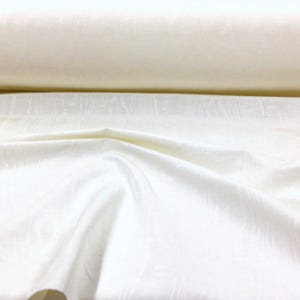 May include: A close-up of a white fabric with a subtle textured pattern. The fabric is smooth and soft, with a slight sheen.