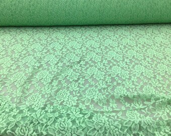 May include: A close-up of a light green floral lace fabric. The lace has a delicate floral pattern and is perfect for crafting and sewing projects.