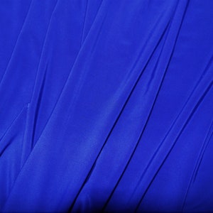 May include: A close-up of a smooth, royal blue fabric with a soft, flowing texture. The fabric is folded and draped, creating a series of diagonal lines.