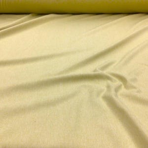 May include: A roll of light yellow fabric with visible folds and creases. The fabric is a solid color and appears to be a soft material. The roll of fabric is in the background.