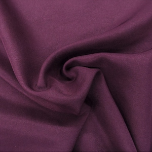 May include: A close-up of a deep purple fabric with a smooth, slightly textured surface. The fabric is folded and draped, creating soft folds and curves.