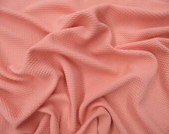May include: A close-up of a peach-colored fabric with a textured waffle-like pattern. The fabric is soft and has a slight sheen.