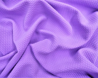 May include: A close-up of a textured, soft, purple fabric. The fabric has a waffle-like texture and is wrinkled and folded.