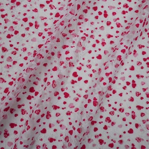 May include: White lace fabric with a pink heart pattern. The fabric is sheer and has a delicate texture.