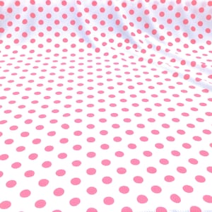 May include: White fabric with a pink polka dot pattern. The fabric is folded and has a slight wrinkle.