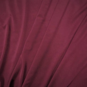 May include: A close-up shot of a draped fabric in a deep burgundy color. The fabric has soft folds and a smooth texture, creating a sense of depth and movement. The lighting highlights the subtle variations in the material.