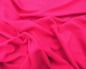 May include: A bright pink textured fabric with a waffle-like pattern. The fabric is folded and draped, showcasing its soft and flexible texture.