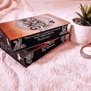 May include: Two paperback books stacked on top of each other. The top book is titled "Fourth Wing" and has a quote on the cover that reads "There's no where in existence you could go that I wouldn't find you Violence". The bottom book is titled "My House, My Chair, My Woman".
