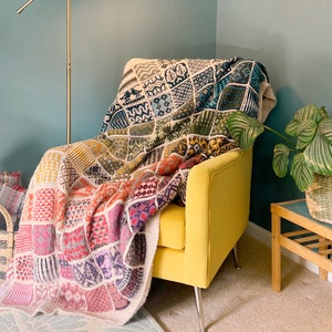 Puede incluir: Un sillón amarillo con una manta de punto de colores drapeada sobre él. La manta está hecha de diferentes cuadrados de tejido de punto en varios colores y patrones. El sillón está en una habitación con una pared verde y una planta en una cesta tejida.