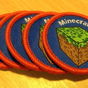 Puede incluir: Cinco parches de Minecraft bordados en azul y rojo con el texto "Minecraft" y un diseño de bloque verde y marrón.