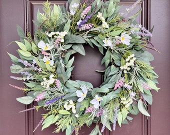 May include: A green, white, and purple floral wreath with a variety of flowers and greenery. The wreath is made of artificial flowers and greenery and is perfect for decorating a door or wall.