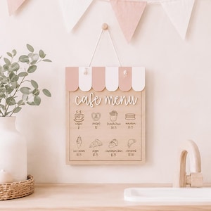 May include: A wooden cafe menu sign featuring a pink and white scalloped awning top. The board displays the text cafe menu and illustrations of food items including coffee, pretzel, french fries, macaron, ice cream, pizza, cinnamon bun, and croissant.