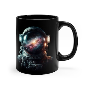 Könnte beinhalten: Schwarze Keramik-Kaffeetasse mit einem Motiv eines Astronautenhelms mit einer Galaxie im Inneren. Der Astronautenhelm ist dunkelgrau mit einem schwarzen Visier. Die Galaxie ist ein wirbelnder Mix aus Blau, Orange und Rosa.