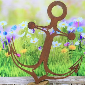 Könnte beinhalten: Eine rostige Metallsilhouette eines Ankers mit einem Sternmuster in der Mitte, die vor einem verschwommenen Hintergrund aus grünem Gras und bunten Blumen steht.