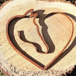 May include: A rusty metal horse head silhouette in the shape of a heart, on a wooden background.