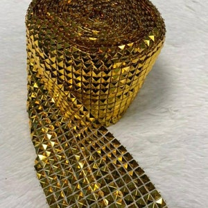 Op de afbeelding: Een rol gouden, glinsterende, ruitvormige trim. De trim is gemaakt van kleine, piramidevormige pailletten.