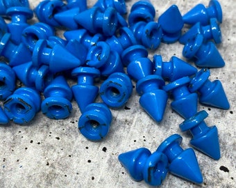 Puede incluir: Un montón de tachuelas de metal azul en forma de pirámide con una base redonda. Las tachuelas tienen un diseño de tornillo en la base.