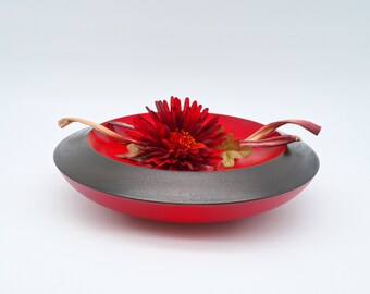 May include: A red wooden bowl with a black rim, featuring a single red flower and dried leaves.