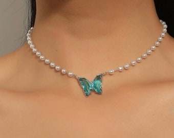 May include: A delicate pearl choker necklace with a blue butterfly pendant. The necklace is made of faux pearls and has a silver chain.
