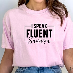 Könnte beinhalten: Ein pinkfarbenes T-Shirt mit dem Aufdruck "Ich spreche fließend Sarkasmus" in Schwarz.